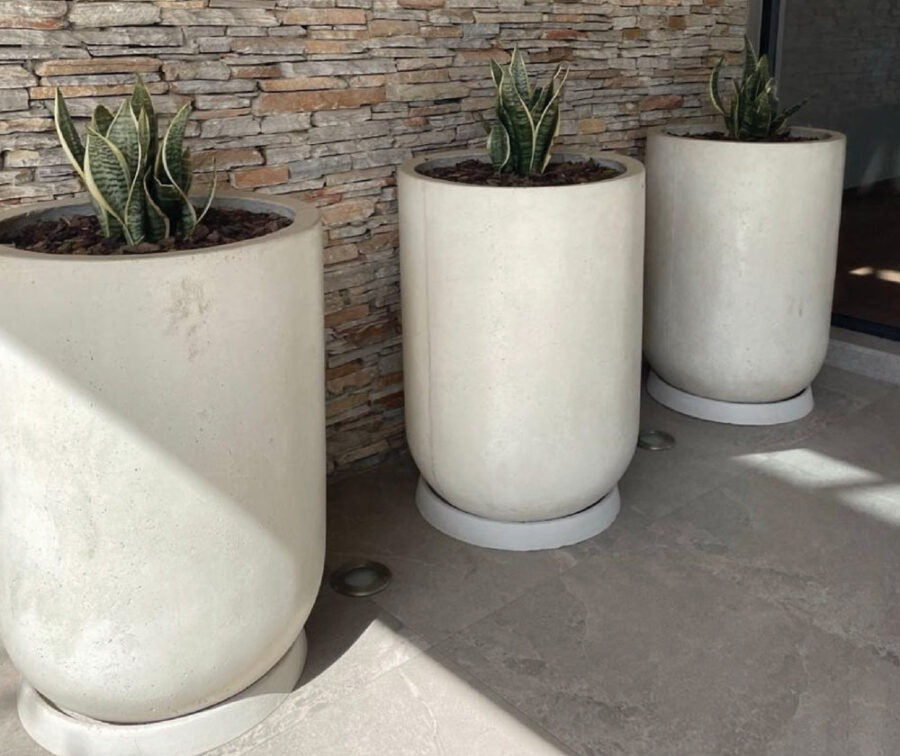 Three tall cream concrete pots planted with grasses on a sunlit stone patio